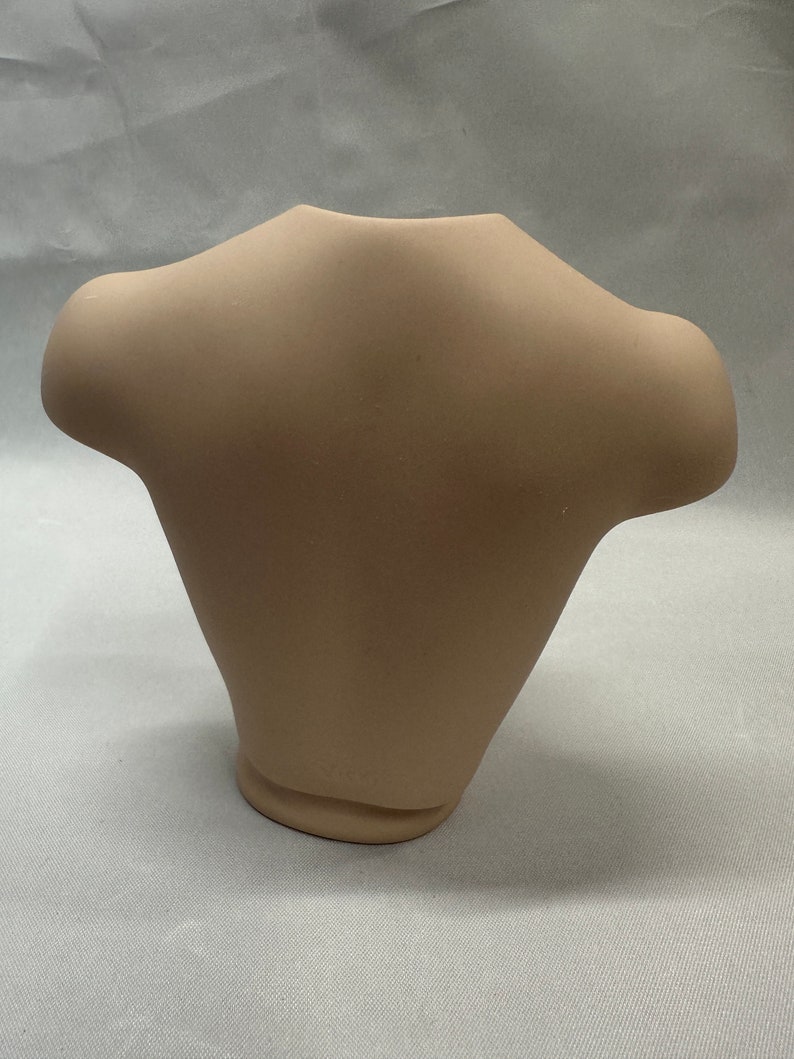 May include: A plain, light brown ceramic torso mannequin for displaying clothing.
