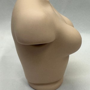 May include: A beige ceramic vase shaped like a torso.