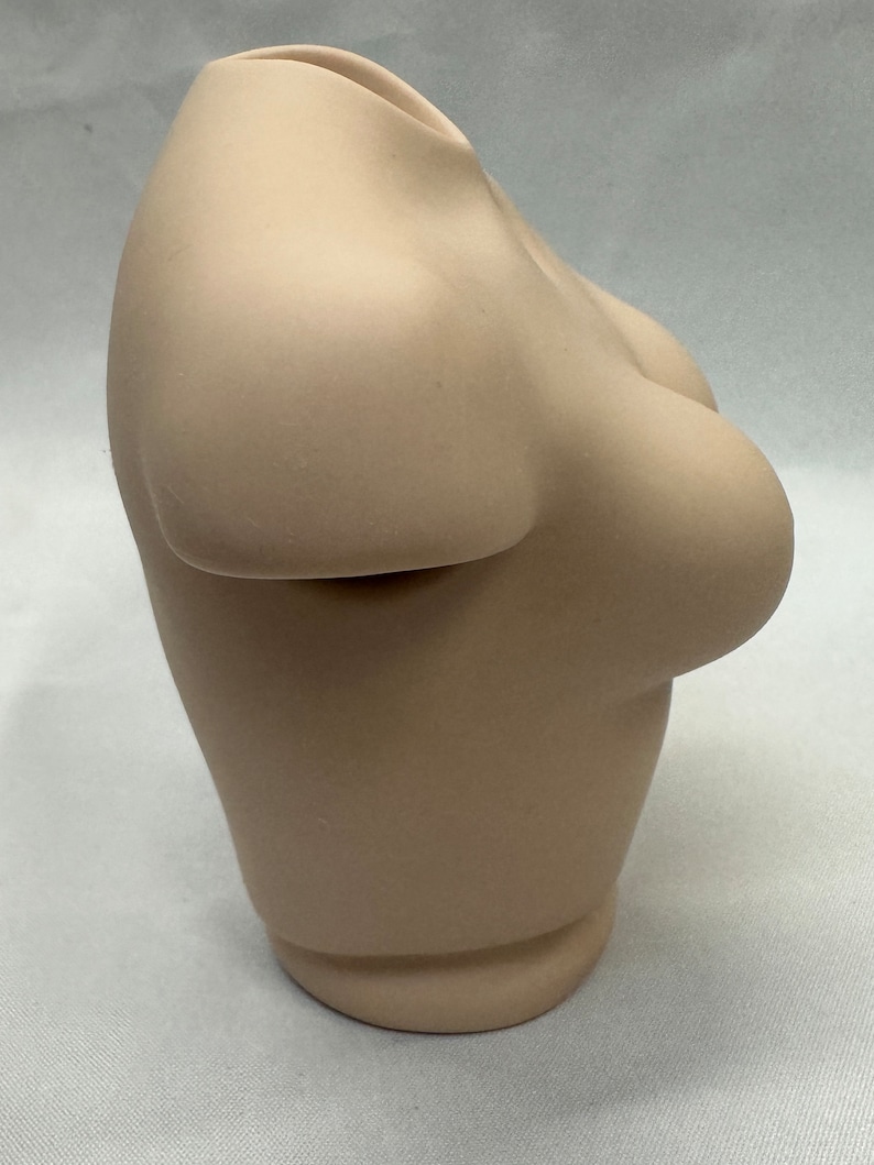 May include: A beige ceramic vase shaped like a torso.