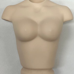 May include: A beige plastic torso mannequin for displaying clothing. The mannequin has a smooth, matte finish and a rounded base.