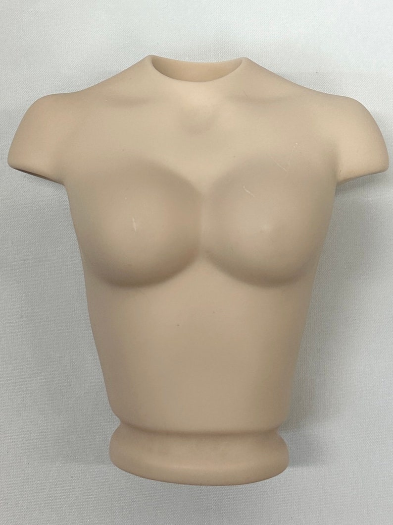 May include: A beige plastic torso mannequin for displaying clothing. The mannequin has a smooth, matte finish and a rounded base.