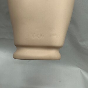 May include: Close-up of the bottom of a white ceramic mannequin head with the text "Vicky Pro" inscribed on the bottom.