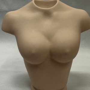 May include: A beige ceramic bust of a person's torso. The bust is smooth and has a rounded shape.