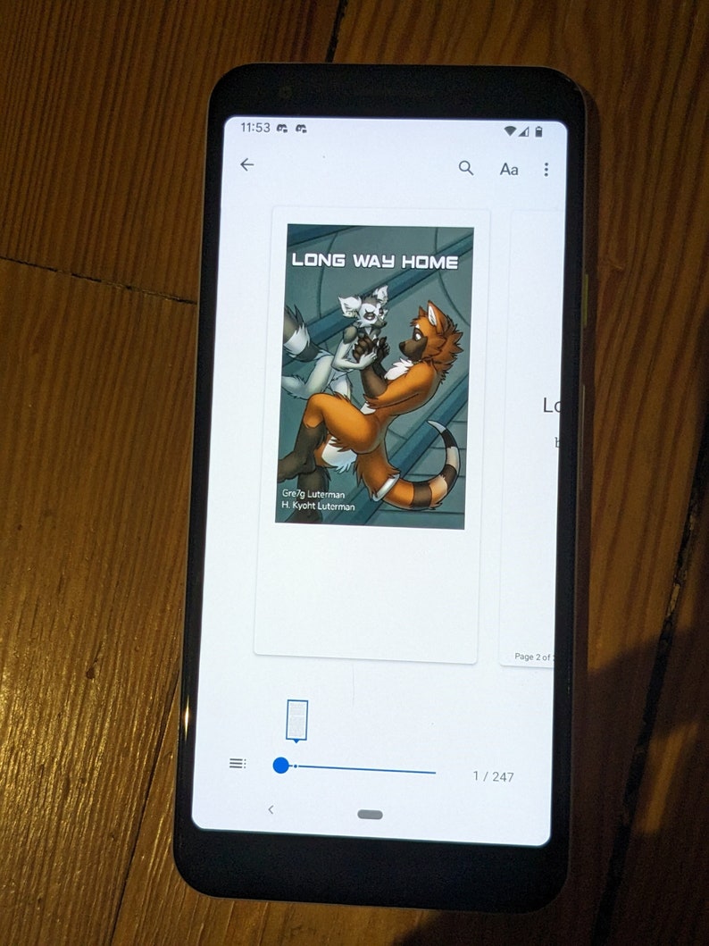 May include: A smartphone displays an ebook cover titled "LONG WAY HOME." The cover art features two anthropomorphic foxes in a dynamic pose. The phone is black and rests on a wooden surface.