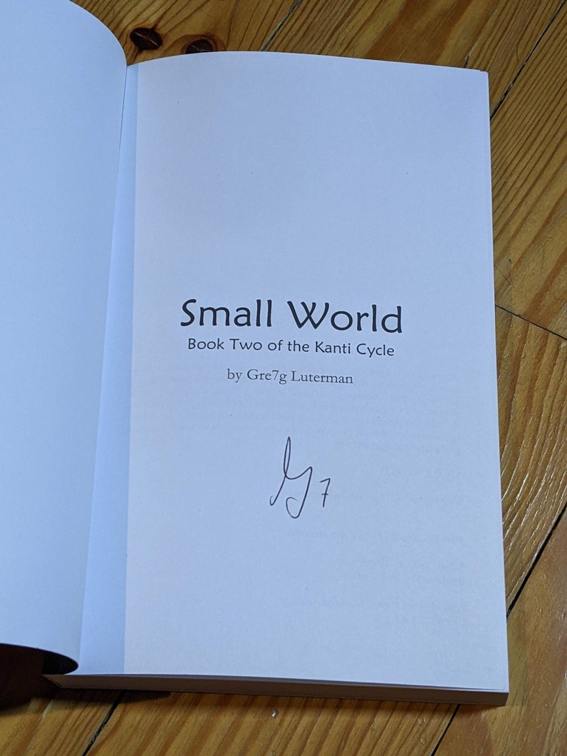 Op de afbeelding: Een wit boek met de titel "Small World" en de ondertitel "Book Two of the Kanti Cycle" door Greg Lutherman. Het boek is gesigneerd met een handgeschreven handtekening.