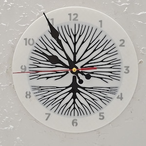 May include: White wall clock with a black tree-of-life design. The clock face features black numerals and hands, with a red second hand. The clock is mounted on a textured white wall.