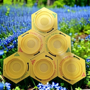 以下が含まれることがあります： 「Decker Colony Apiary」の文字と蜂のグラフィックが入った黄色の六角形の養蜂器具。 器具はハニカム模様に配置され、青い花と緑の葉の背景に配置されています。
