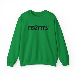 Puede incluir: Sudadera verde con la palabra "TESTIFY" impresa en negro en la parte delantera.