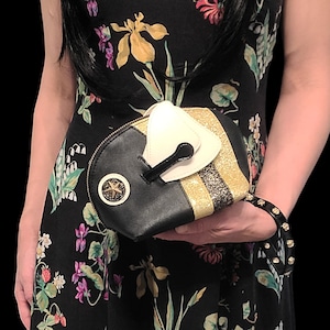 May include: A black and gold bee-shaped clutch purse with a white, 3D bee head detail. The purse has a gold glitter stripe and a black star on the front.