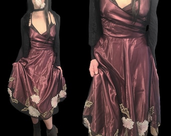 May include: A burgundy satin dress with floral embroidery and a black lace trim. The dress has a sweetheart neckline and a fitted bodice. The skirt is full and flowing.