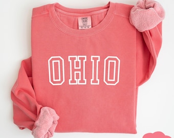 May include: A coral pink sweatshirt with the word "OHIO" in white outlined letters. The sweatshirt is folded in half and the sleeves are rolled up.