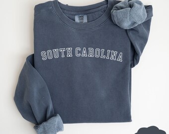 May include: A dark blue sweatshirt with the text "SOUTH CAROLINA" in white outlined letters. The sweatshirt is folded and the sleeves are rolled up.