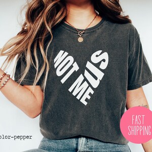 May include: A dark gray cropped t-shirt with a white graphic that says "Not Me Sis" in a heart shape.