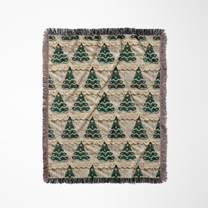 May include: A woven throw blanket with a cream background and a repeating pattern of green Christmas trees with white lace trim.