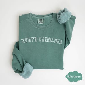 May include: A light green sweatshirt with the text "NORTH CAROLINA" in white outlined letters.