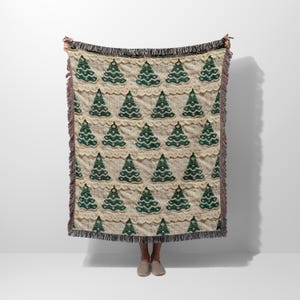 May include: A cream-colored woven throw blanket with a repeating pattern of green Christmas trees. The blanket has a fringe border.