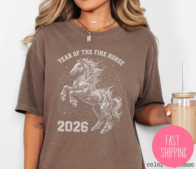 K&ouml;nnte beinhalten: Braunes T-Shirt mit einer wei&szlig;en Illustration eines sich aufb&auml;umenden Pferdes mit feuriger M&auml;hne und dem Text "YEAR OF THE FIRE HORSE 2026". Das Design ist auf dem T-Shirt zentriert.