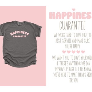 May include: A gray t-shirt with the text "Happiness Guarantee" in pink letters. The text is in a retro font style.
