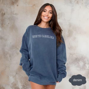 May include: A blue sweatshirt with the text "NORTH CAROLINA" in white outlined letters. The sweatshirt is made of a soft, comfortable fabric and has a relaxed fit.
