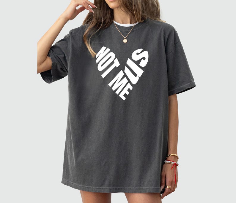 May include: A dark gray oversized t-shirt with a white graphic of a heart formed by the words "Not Me Sis".