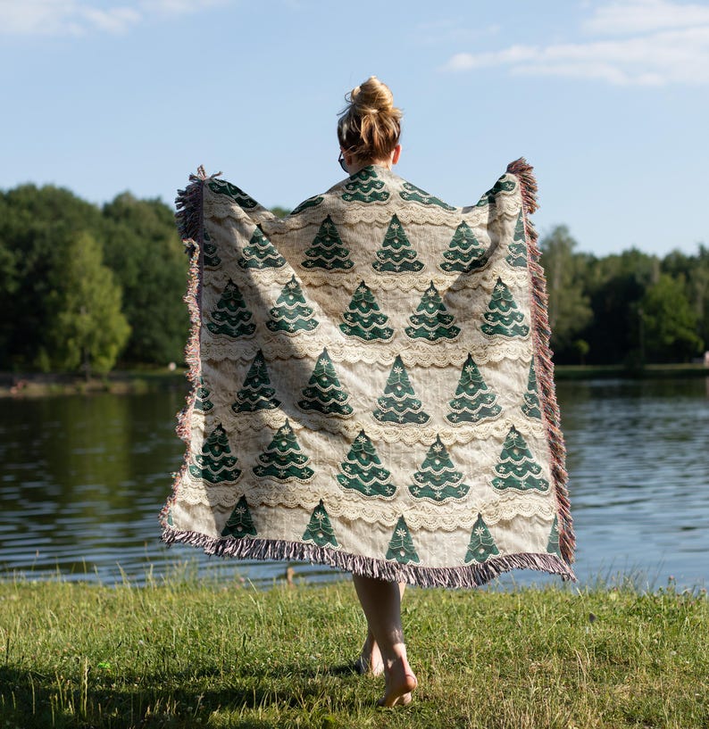 May include: A person holding a woven throw blanket with a green and white Christmas tree pattern. The blanket has fringe on the edges.