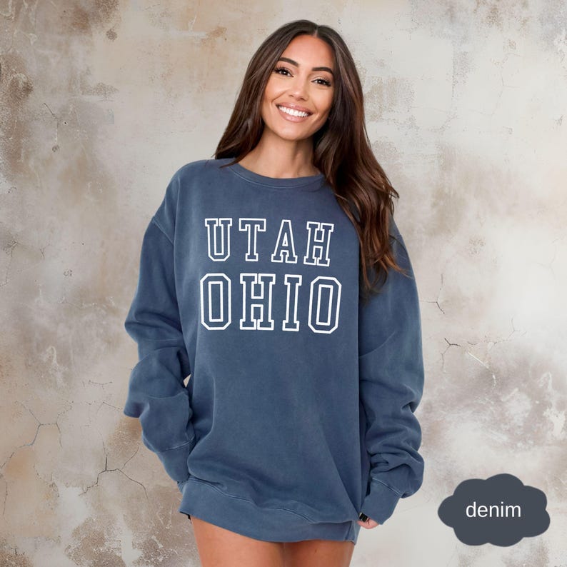 May include: A dark blue sweatshirt with the text "UTAH OHIO" in white outlined letters. The sweatshirt is made of a soft, comfortable fabric and has a relaxed fit.