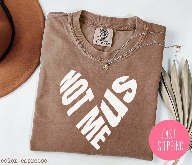 May include: A brown t-shirt with the text "Not Me Sis" printed in white in a heart shape.