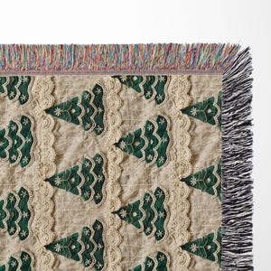 May include: A cream-colored throw blanket with a repeating pattern of green embroidered Christmas trees. The blanket has a fringe border.