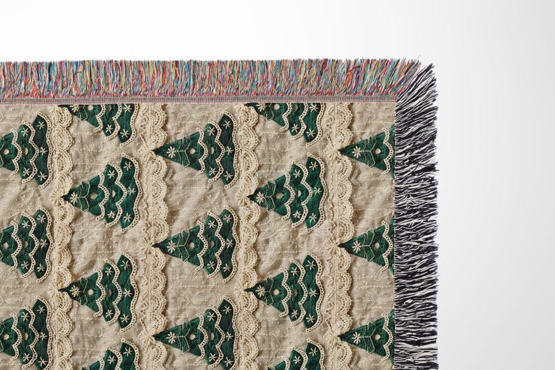 May include: A cream-colored throw blanket with a repeating pattern of green embroidered Christmas trees. The blanket has a fringe border.
