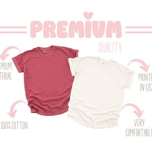 May include: Two blank t-shirts, one in a dusty rose color and one in white, with the text "PREMIUM QUALITY" and "PRINTED IN USA" in pink. The text "PREMIUM MATERIAL", "100% COTTON", and "VERY COMFORTABLE" are also included.