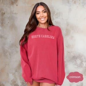 May include: A crimson red sweatshirt with the text "NORTH CAROLINA" in white outlined letters.