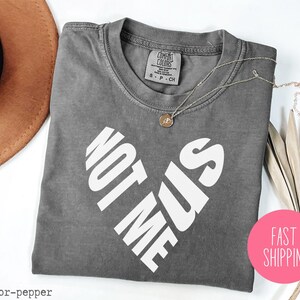 May include: Gray t-shirt with a white heart design that says "Not Me Sis".