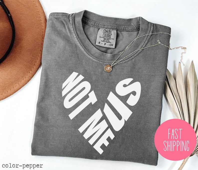 May include: Gray t-shirt with a white heart design that says "Not Me Sis".