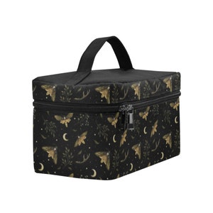 May include: Black cosmetic bag with a repeating pattern of gold moths, crescent moons, and foliage. The bag has a black handle and zipper. The design is set against a black background.