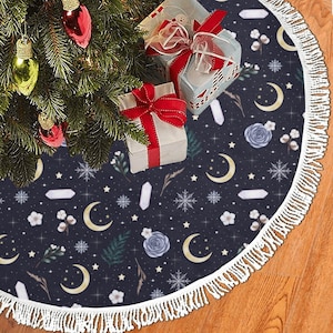 May include: A dark blue Christmas tree skirt featuring a celestial design of moons, stars, crystals, and snowflakes. The skirt has a white fringe trim and is decorated with gifts and ornaments.
