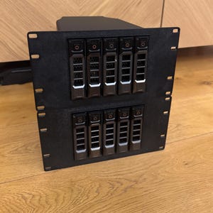 May include: A black server rack with multiple hard drives installed. The rack is made of metal and has a sleek, modern design.