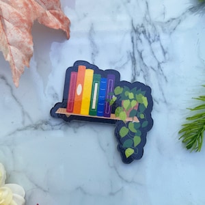 Rainbow colored books on a floating shelf with house plant.