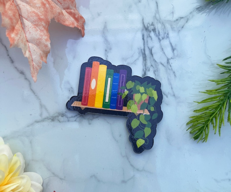 Rainbow colored books on a floating shelf with house plant.
