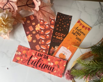 May include: Set of five autumn-themed bookmarks with various designs. One bookmark features a pumpkin and candle with the text "Autumn Vibes Save Lives". Another bookmark has a brown background with a pattern of coffee cups, pie, and pumpkins. Another bookmark has a brown background with a pattern of leaves. Another bookmark has a red background with a pattern of pumpkins, leaves, and flowers with the text "I am an Autumn". The last bookmark has a brown background with a pattern of coffee cups, pie, and pumpkins with the text "Cozy and Come".