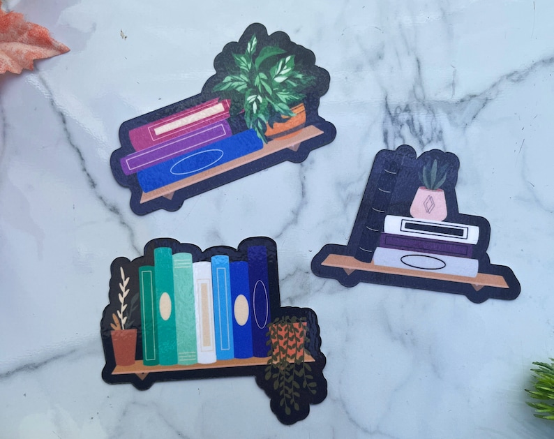 3 subtle pride stickers. Bisexual, horizontal pink, purple and blue books with a plant. Demisexual, upright black, horizontal white, purple and grey books with a succulent on top. Gay, range of teal to white to blue books with a plant on both sides.