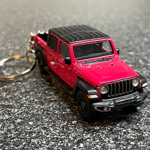 May include: A red and black toy pickup truck keychain. The miniature vehicle features a detailed design with a black roof, black wheels, and a silver key ring. The truck is a vibrant red color.