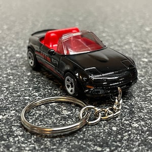 May include: Black toy car keychain with red interior and a silver chain. The car is a convertible and has a detailed design.