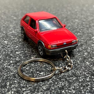 May include: Red Ford Fiesta keychain with a silver key ring and chain. The car is a miniature replica of a Ford Fiesta.