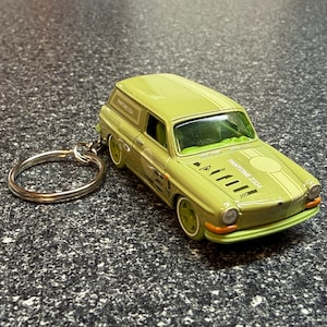 May include: A light green die-cast toy car keychain featuring a station wagon body style. The vehicle has white racing stripes, the text PANTONE 2304 on the hood and side, and a silver metal split ring attached to the rear for keys.