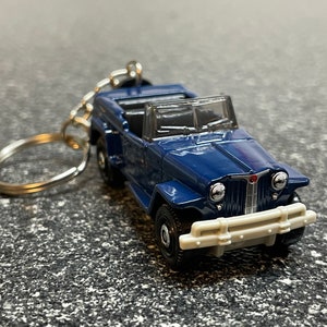 May include: A blue toy car keychain with a silver key ring. The car is a vintage-style convertible with a detailed front grill and headlights.