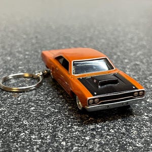 May include: Orange and black die-cast model car keychain. The miniature car features a detailed design with a black hood and silver accents. The keychain includes a silver split ring for attaching to keys or bags.