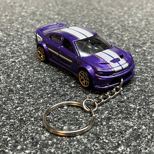 May include: A purple Dodge Charger diecast car with white racing stripes, gold wheels, and a silver keychain attached.