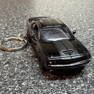 May include: A black die-cast model car keychain with a silver key ring. The car has black racing stripes on the hood and roof. The car's details include headlights, a front grill, and side mirrors.