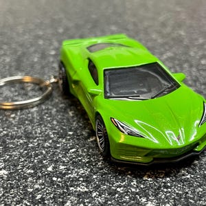 May include: A bright green toy sports car keychain. The miniature car has detailed headlights, a windshield, and a silver key ring. The car is approximately 3 inches long.