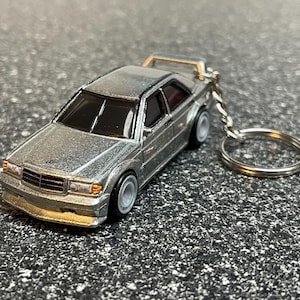 May include: A silver Mercedes-Benz 190E keychain with a black interior and a silver key ring.